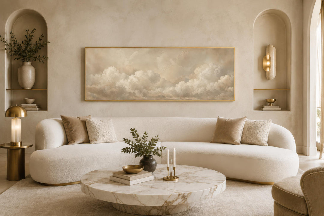 Long narrow horizontal canvas art of soft beige clouds above a curved white sofa in a neutral room.