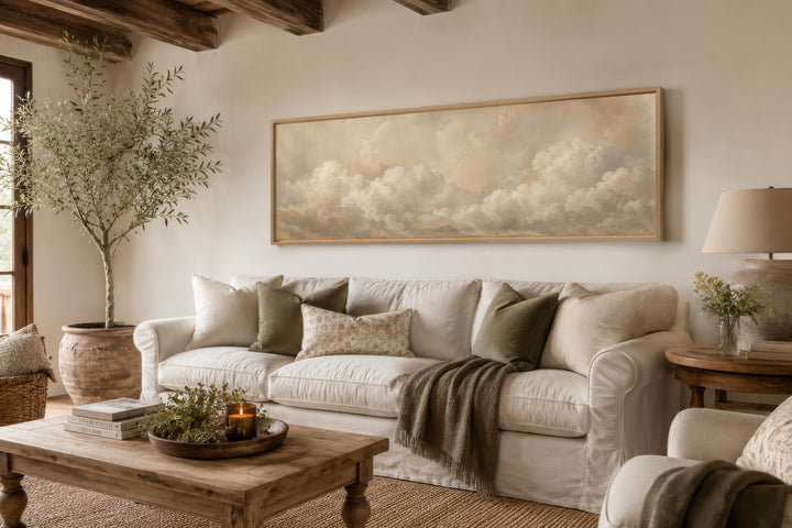 Long horizontal wall art featuring soft beige and white clouds above a white sofa in a cozy room.