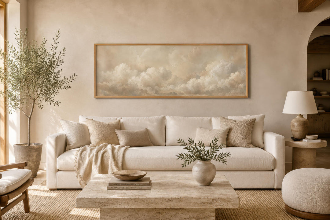 Long narrow horizontal wall art featuring soft beige and white clouds in a wooden frame above a sofa