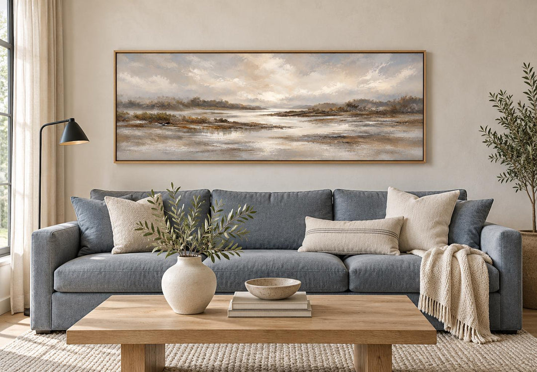 Neutral earth tones river landscape long horizontal canvas wall art above a blue sofa.
