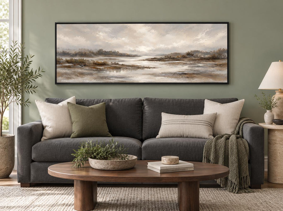 Neutral earth tones river landscape long horizontal canvas wall art above a dark gray sofa.