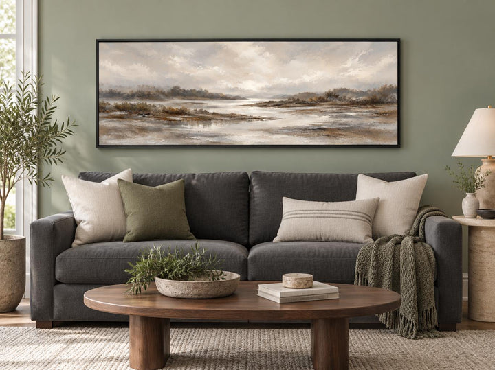 Neutral earth tones river landscape long horizontal canvas wall art above a dark gray sofa.
