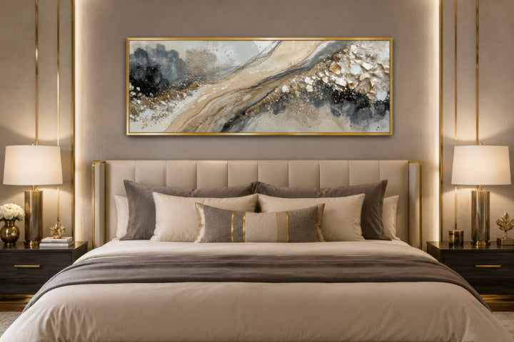Long horizontal abstract canvas wall art in neutral grey, beige, and gold above a modern bed.