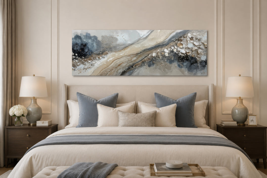 Long horizontal abstract canvas wall art in neutral grey, beige, and gold above a bed.