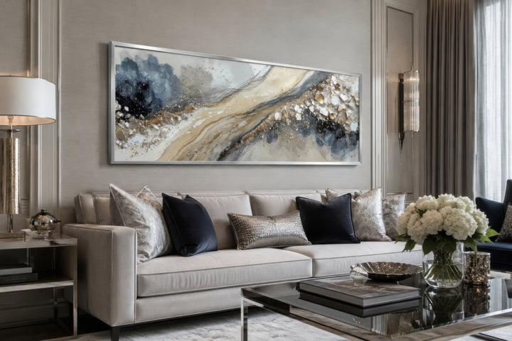 Long horizontal abstract canvas wall art in neutral grey, beige, and gold above a modern sofa.