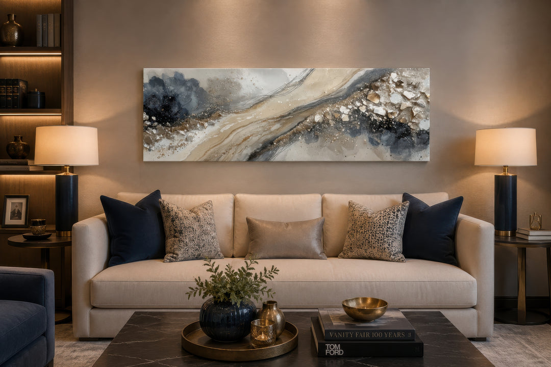 Long horizontal abstract canvas wall art in neutral grey, beige, and gold above a modern couch.