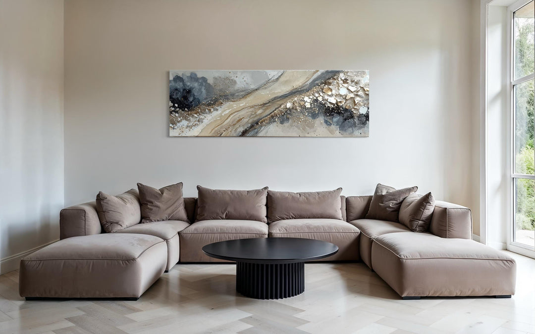 Long horizontal abstract canvas wall art with grey, beige, and gold tones above a modern sofa.