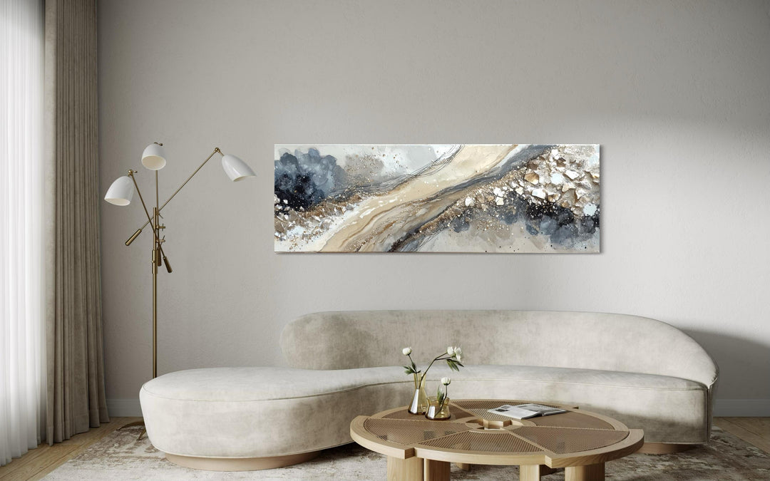 Long horizontal abstract canvas wall art in neutral grey, beige, and gold above a curved sofa.