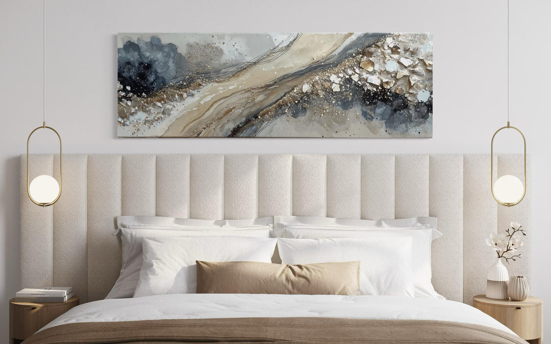 Long horizontal abstract canvas wall art in neutral grey, beige, and gold above a modern bed.