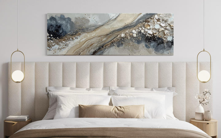 Long horizontal abstract canvas wall art in neutral grey, beige, and gold above a modern bed.