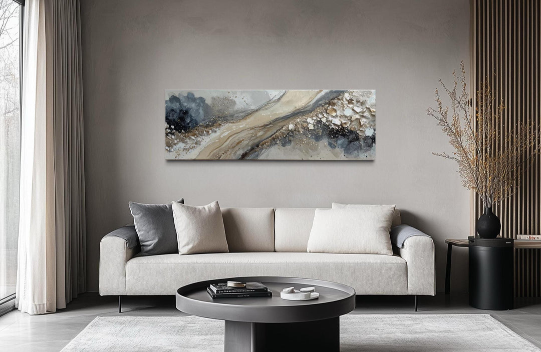 Long horizontal abstract canvas wall art in neutral grey, beige, and gold above a modern sofa.