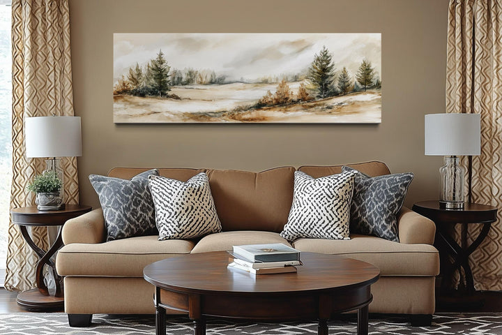 Panoramic canvas print of a neutral landscape in beige, brown, and green above a tan sofa.