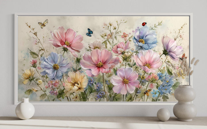 Neutral pink and blue wildflower wall art with butterflies and ladybugs in a white frame.