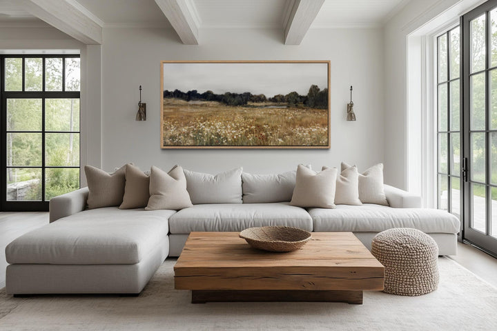 Neutral wildflower field landscape canvas wall art in a wood frame above a sofa in a living room.