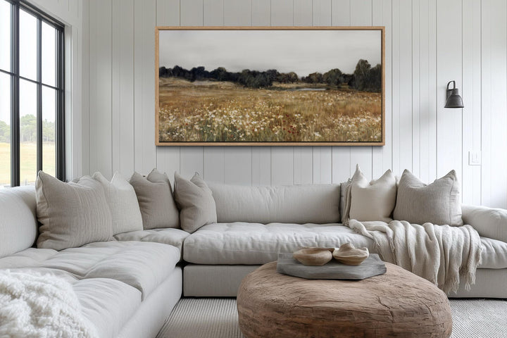 Neutral wildflower field landscape canvas wall art in a wood frame above a modern sectional sofa.