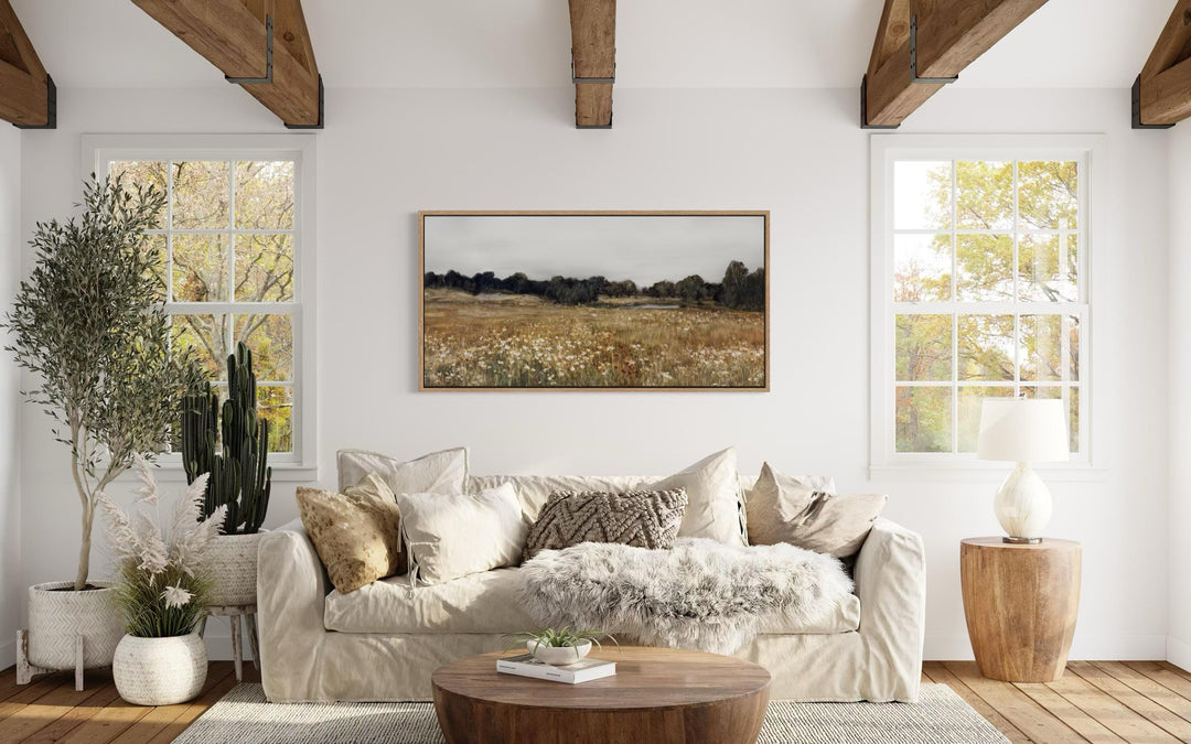 A horizontal canvas print of a neutral wildflower field landscape hangs in a farmhouse living room.