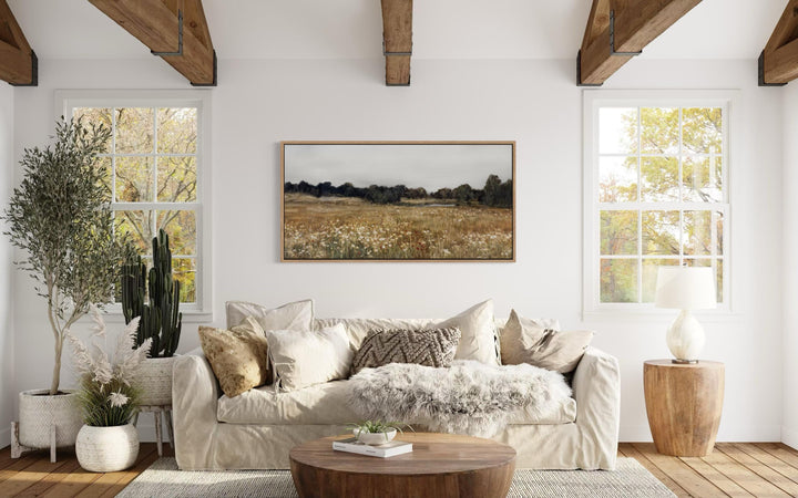 A horizontal canvas print of a neutral wildflower field landscape hangs in a farmhouse living room.