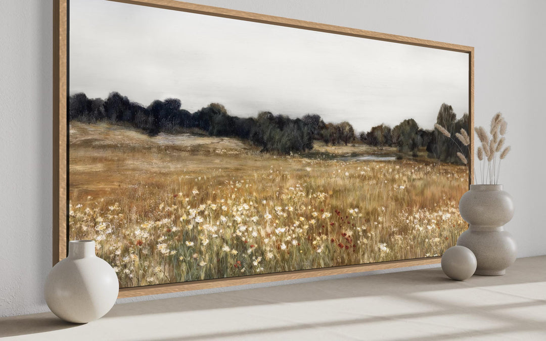 Neutral wildflower field landscape canvas wall art in a wood frame above a shelf with vases.