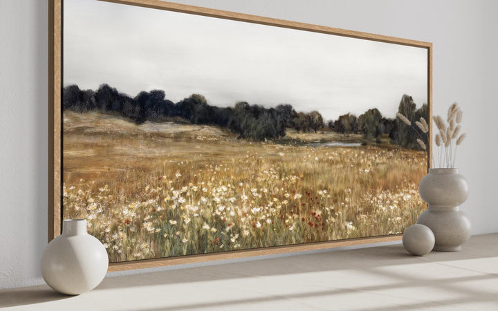 Neutral wildflower field landscape canvas wall art in a wood frame above a shelf with vases.