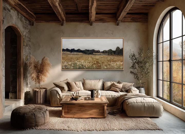 A horizontal canvas print of a neutral wildflower field landscape hangs in a rustic living room.