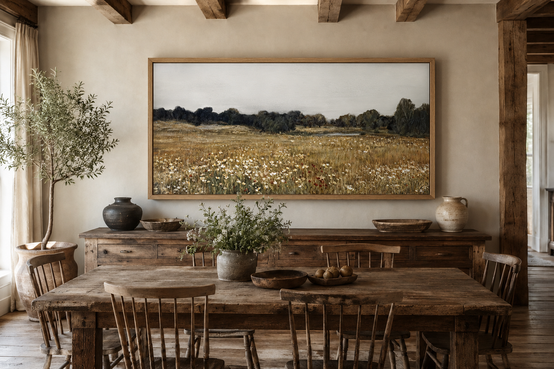 Neutral wildflower field landscape canvas wall art in a rustic frame above a wooden sideboard.