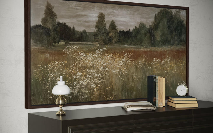 Neutral wildflower meadow canvas print in a dark wood frame above a dresser with vintage decor.
