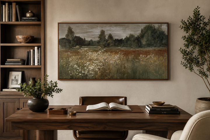 Neutral wildflower meadow canvas print in a dark wood frame above a rustic wooden desk.