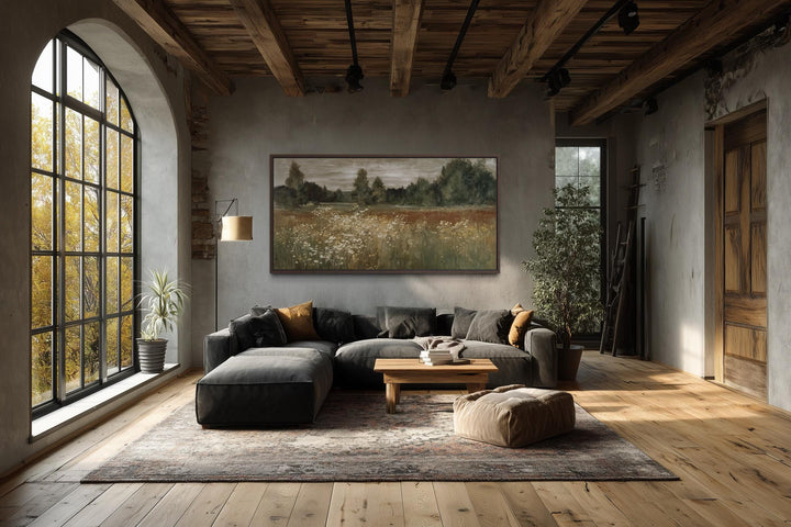 Neutral wildflower meadow canvas wall art in a rustic farmhouse living room above a dark sofa.