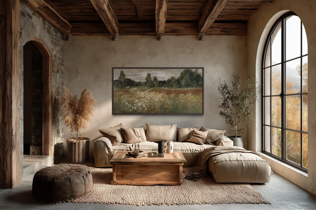 A wide canvas print of a neutral wildflower meadow landscape hangs in a rustic farmhouse living room.