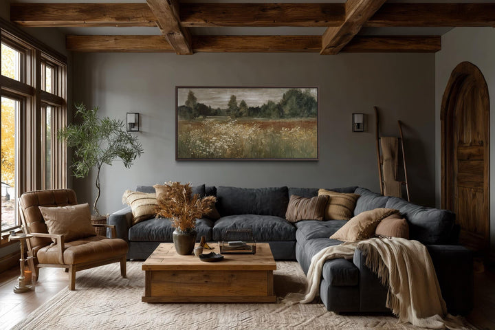 Neutral wildflower meadow canvas wall art in a rustic farmhouse living room above a dark sofa.