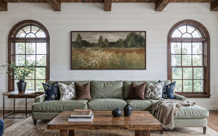 A framed canvas print of a neutral wildflower meadow landscape hangs above a green sofa.