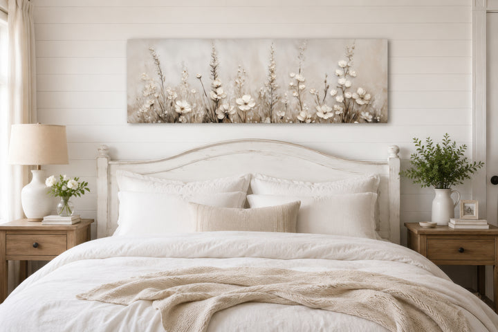 Neutral wildflower canvas print in beige and cream tones hanging above a white wooden bed frame.