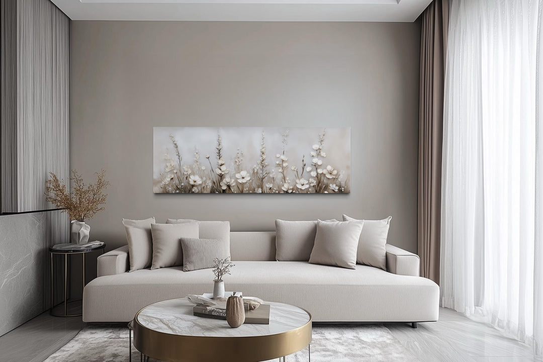 Horizontal canvas print of neutral wildflowers in beige and ivory tones above a modern sofa.