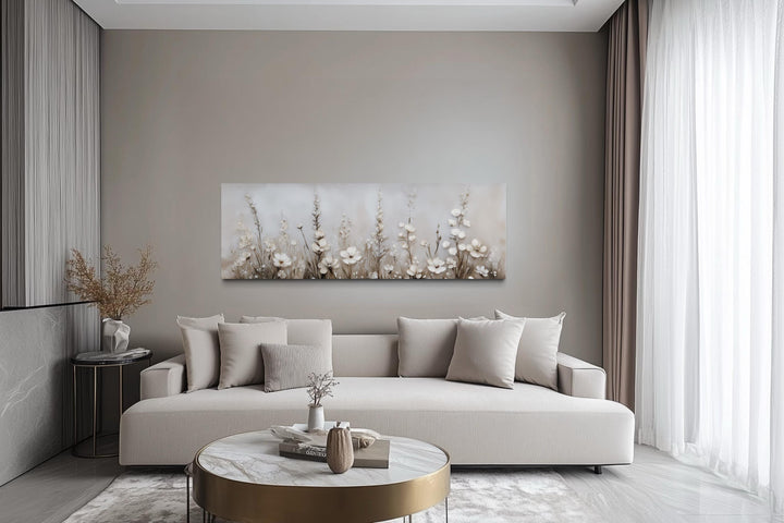 Horizontal canvas print of neutral wildflowers in beige and ivory tones above a modern sofa.