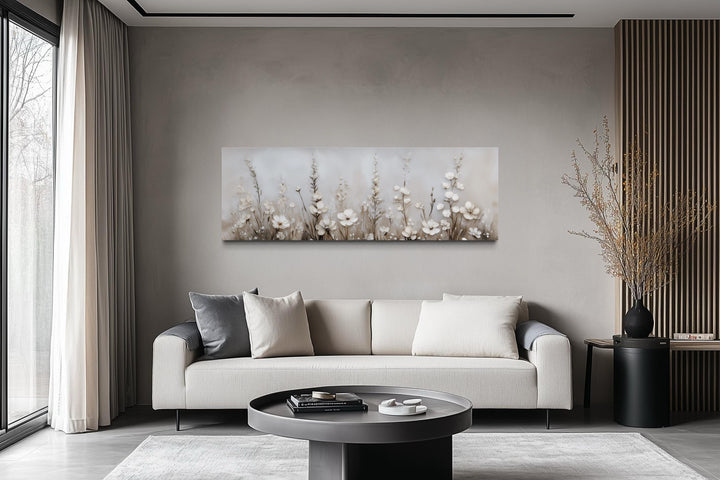 Horizontal canvas print of neutral wildflowers in beige and ivory tones above a modern sofa.