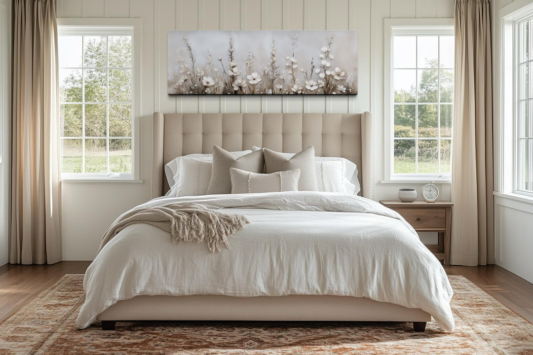 Horizontal canvas print of neutral wildflowers hanging above a bed in a serene, beige bedroom.