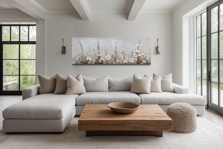 Horizontal canvas print of neutral wildflowers in a beige living room above a light gray sofa.
