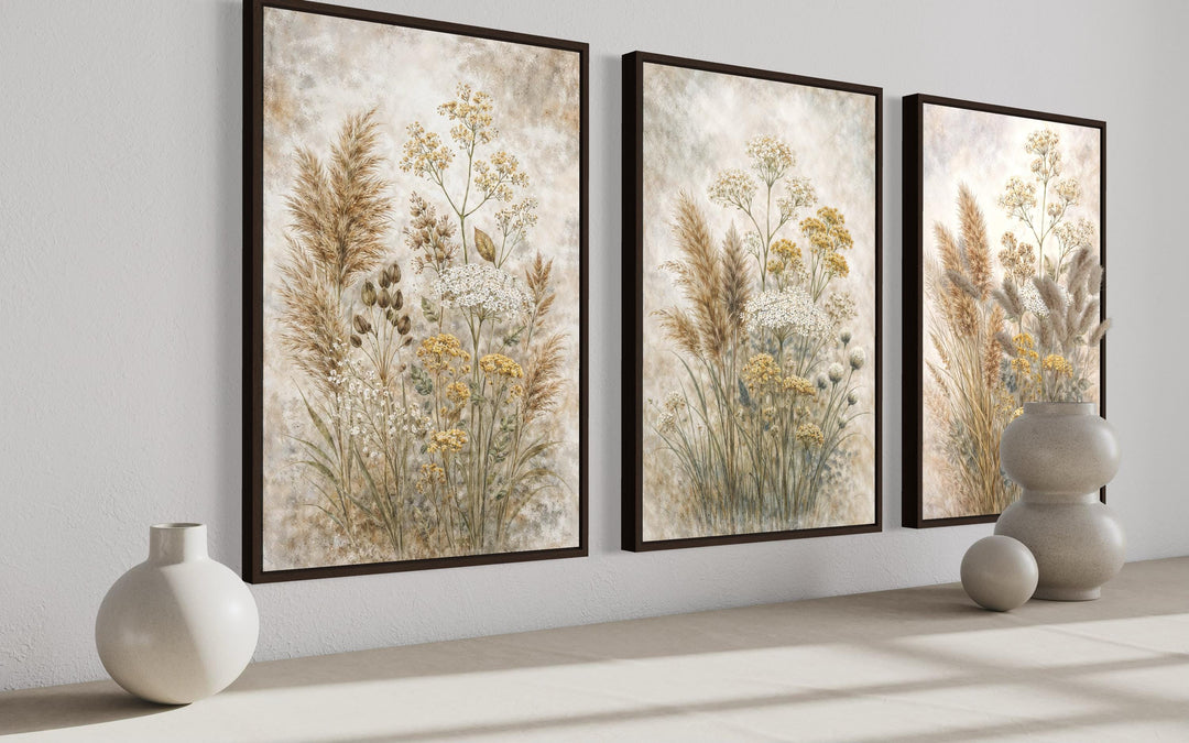 Set of three neutral wildflower botanical canvas prints in dark frames on a white wall.