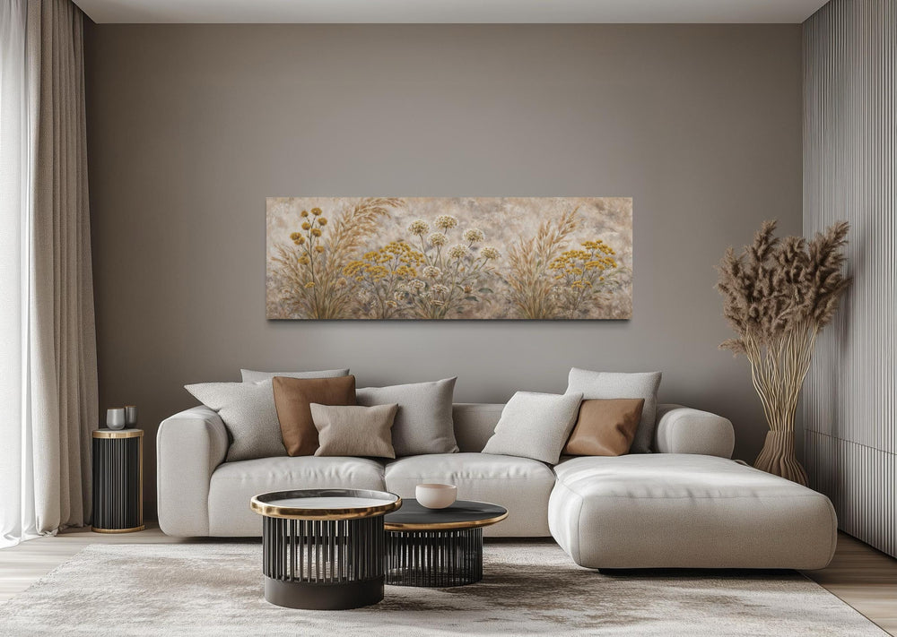 A long narrow canvas print of neutral wildflowers hangs above a modern sofa in a minimalist room.