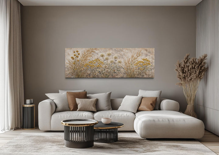 A long narrow canvas print of neutral wildflowers hangs above a modern sofa in a minimalist room.