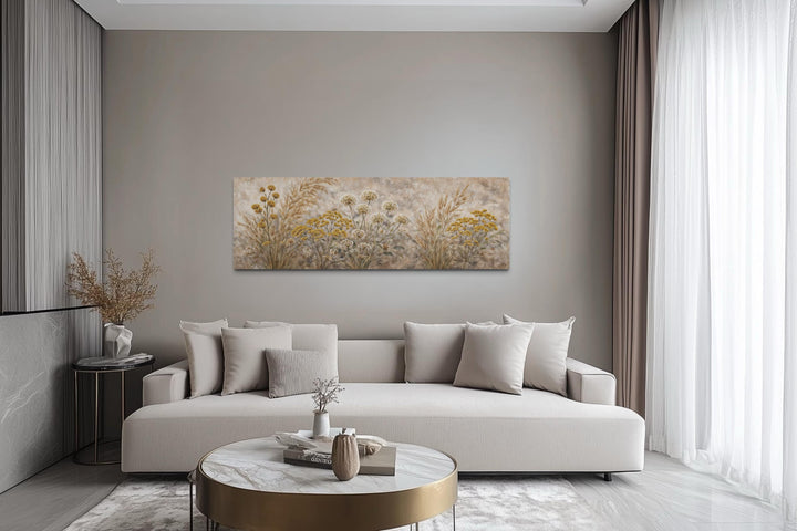 A long narrow canvas print of neutral wildflowers and meadow grasses hangs above a modern sofa.