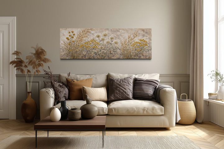 A long narrow canvas print of neutral wildflowers and meadow grass hangs above a beige sofa.