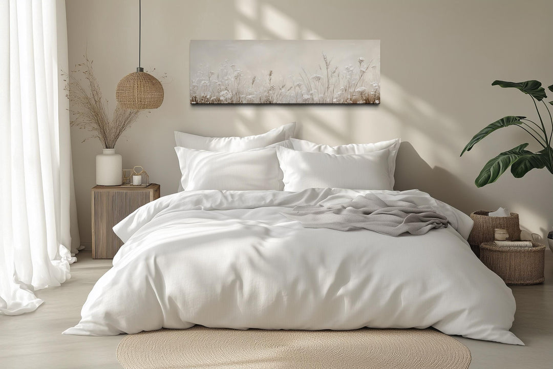 Horizontal beige botanical canvas print of wildflowers above a bed in a neutral-toned room.