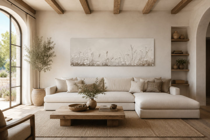 Horizontal beige botanical canvas print of wildflowers and meadow grasses above a white sofa.