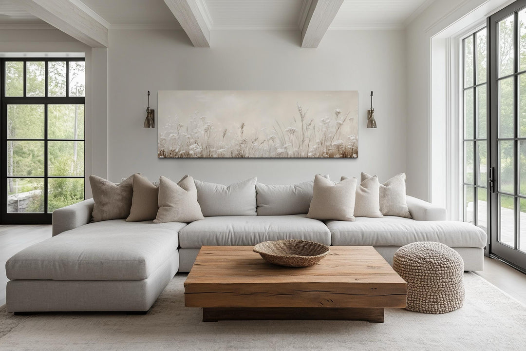 Horizontal beige botanical canvas print of wildflowers above a sofa in a neutral living room.