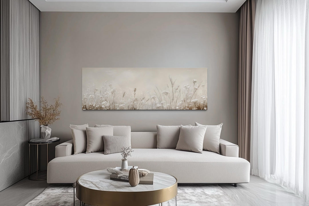 Horizontal canvas print of neutral wildflowers and meadow grasses above a beige sofa.