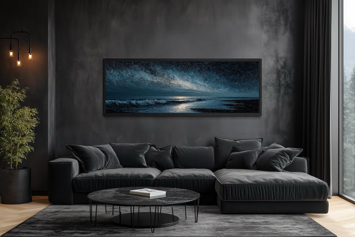Panoramic dark blue seascape canvas print with a starry sky above a modern black sofa.
