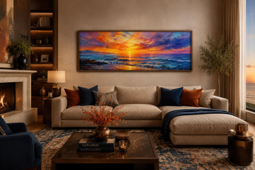 Long horizontal canvas art of a fiery ocean sunset with purple and orange sky above a beige sofa.