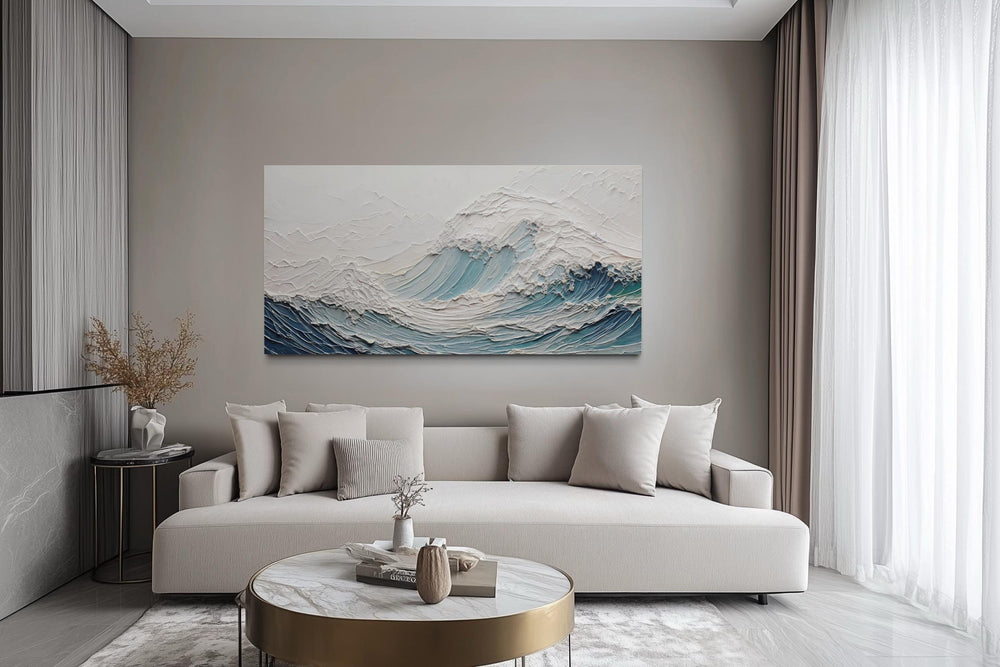 A large horizontal canvas of a textured teal ocean wave hangs above a modern neutral sofa.