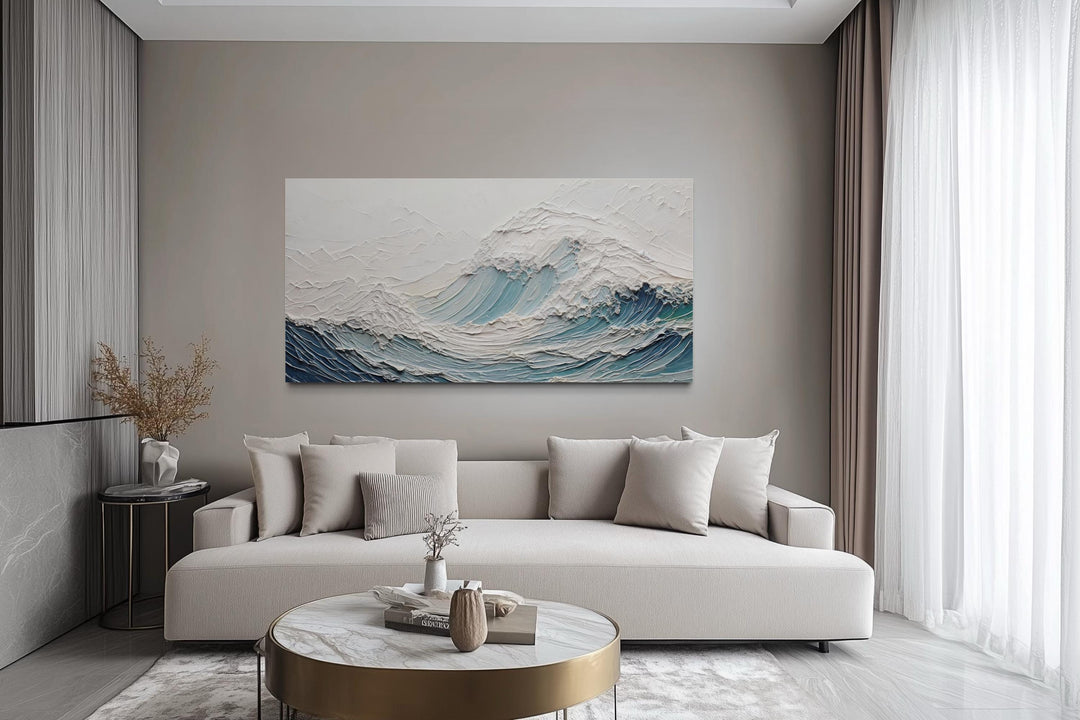 A large horizontal canvas of a textured teal ocean wave hangs above a modern neutral sofa.